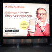 Shop Apotheke: Ärger wegen Jauch-Spot Das Foto zeigt ein Werbeplakat des Versenders ShopApotheke. TV-Moderator Günther Jauch hält ein Handy hoch, auf dem die ShopApotheke-App geöffnet ist. Er hält eine Gesundheitskarte von hinten an das Gerät. Auf dem Plakat steht: „E-Rezept? Einfach ShopApotheke-App. Jetzt herunterladen und Wege sparen.“