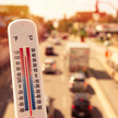 Starke Hitze: Gefahr für Menschen und Medikamente Symbolbild: Das Foto zeigt im Vordergrund ein Thermometer. Im Hintergrund ist eine sonnenbeschienene, mehrspurige und stark befahrene Straße zu sehen.