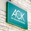 Einzelimport auch ohne Genehmigung Symbolbild: AOK-Logo auf einem Schild an einer Fassade.