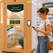 Assistierte Telemedizin: Doctorbox steigt ein Frau am Handy steht vor der Doctorbox-Kabine in einer Apotheke