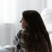 Angststörungen seit Corona: Anstieg „besorgniserregend“ Foto: Eine junge Frau sitzt auf einem Bett und schaut nach links