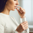 Perimenopause: Welche Supplemente sind sinnvoll? Foto: Eine Frau im Profil hält eine Tablette vor ihre Lippen und hält ein Glas Wasser in ihrer Hand.