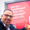 Regionales Marketing: Gesund.de zeigt Apotheker vor Ort Oliver Hildebrandt vor seinem Gesund.de-Plakat